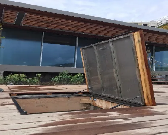 Stainless plant room cover clad in timber decking, held open on its damper