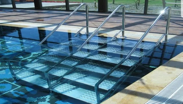 Stainless steel pool ladder installed in a deck-level pool, with non-slip patterned wide treads and Ø42 mm bright stainless handrails