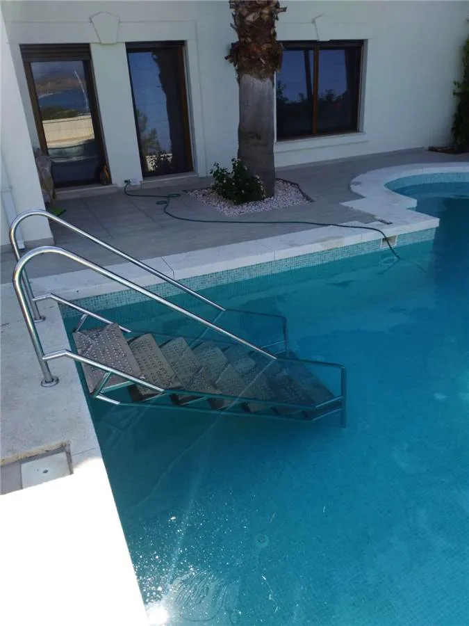 Stainless steel pool ladder in a villa pool — wide-tread model, anchored to the pool coping