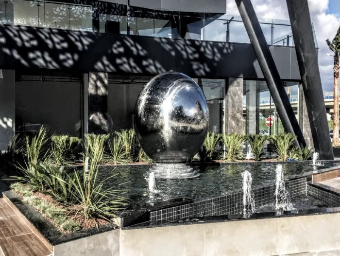 Polished stainless steel water sphere in an ornamental pool with a surrounding group of foam jets